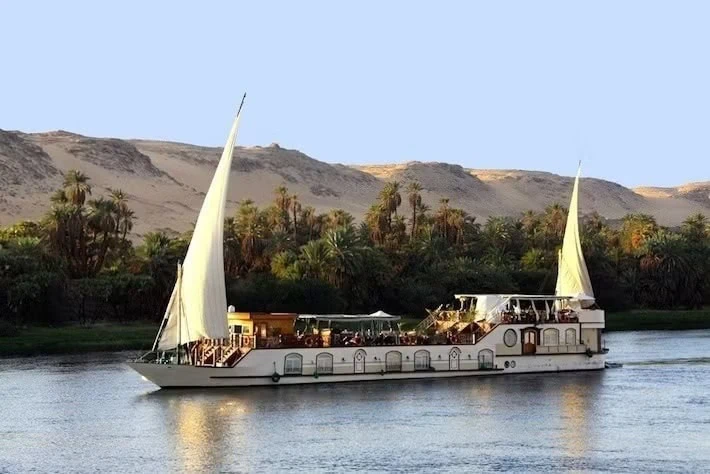 Nile River landscape with sailboat, palm trees and lush vegetation along the riverbank