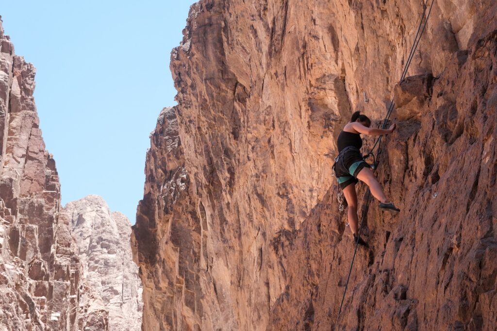 Woman climbing a rock formation in a desert landscape, Dahab