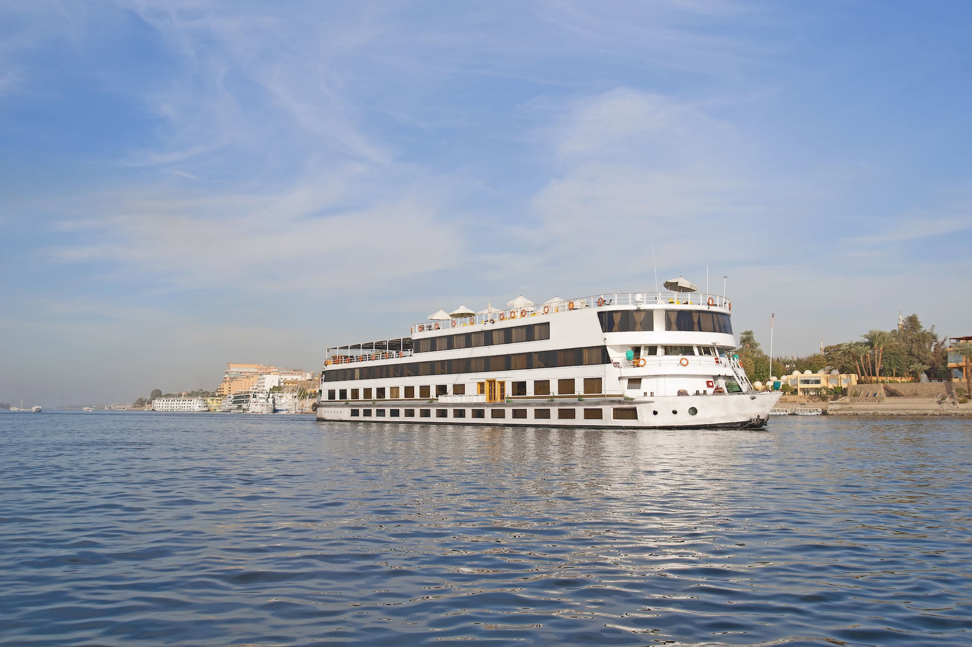 Cruise ship on the Nile River in Aswan with palm trees and buildings along the shore