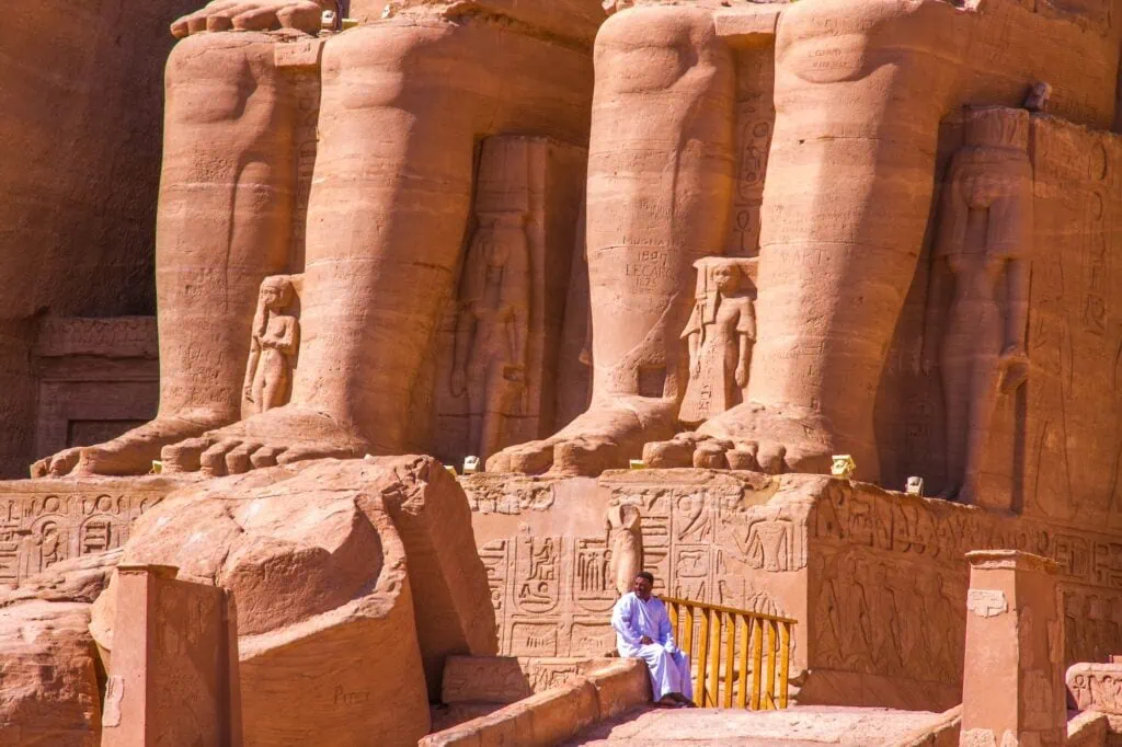 A uniformed local guard standing at the entrance of the Great Temple of Ramesses II at Abu Simbel, with one of the four colossal seated statues rising behind him, Egypt.