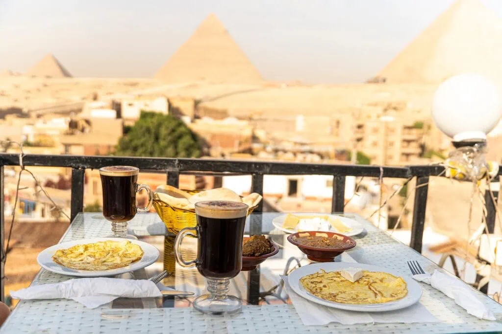 Outdoor restaurant table set for a meal on a rooftop terrace in Cairo with the three Great Pyramids of Giza visible in the background