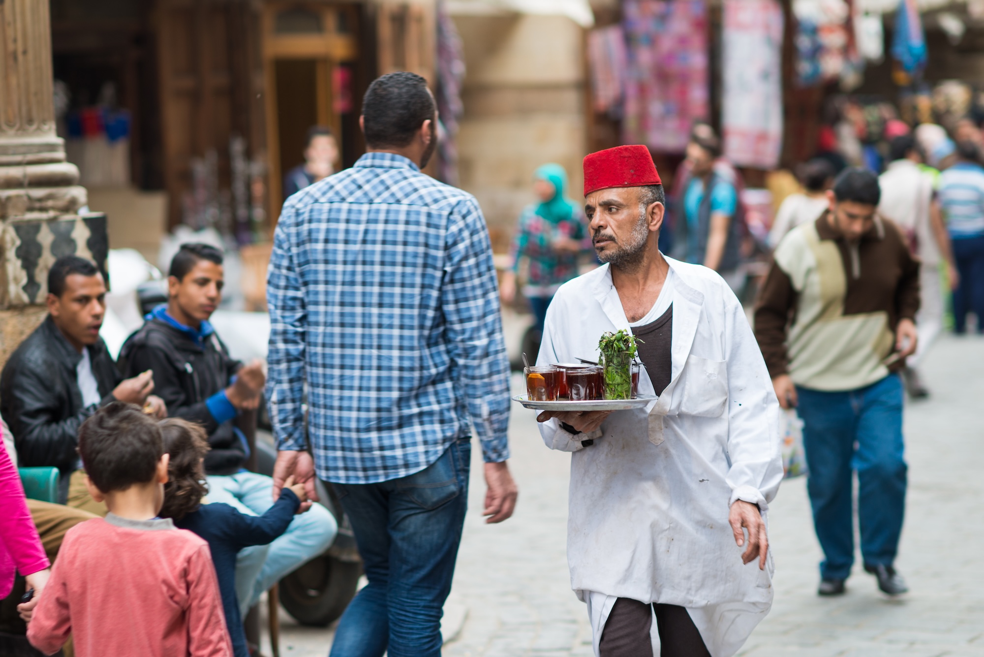 Tea house servant carrying traditional tea glasses through Khan Al-Khalili bazaar