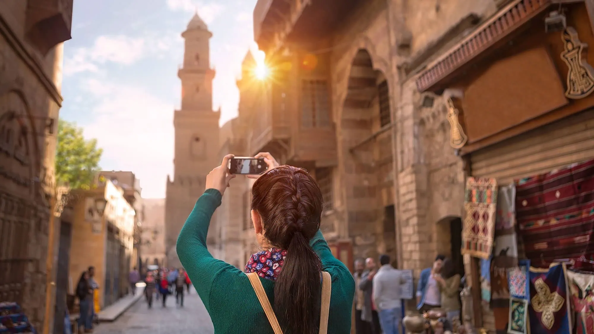 Turista con smartphone nel vivace bazar storico del Cairo islamico con minareti e architettura tradizionale