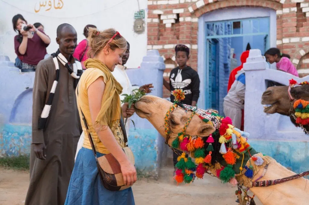 A traveler in a colourful Nubian village near Aswan feeding a camel beside the painted exterior walls of traditional houses
