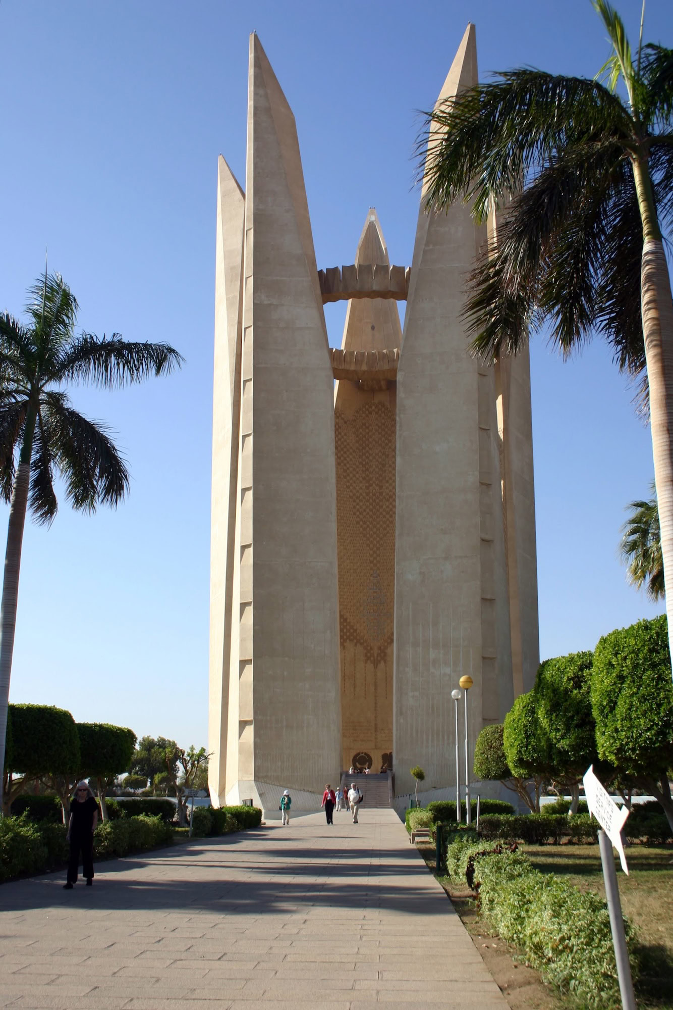 Aswan High Dam monument with palm trees and visitors on walkway