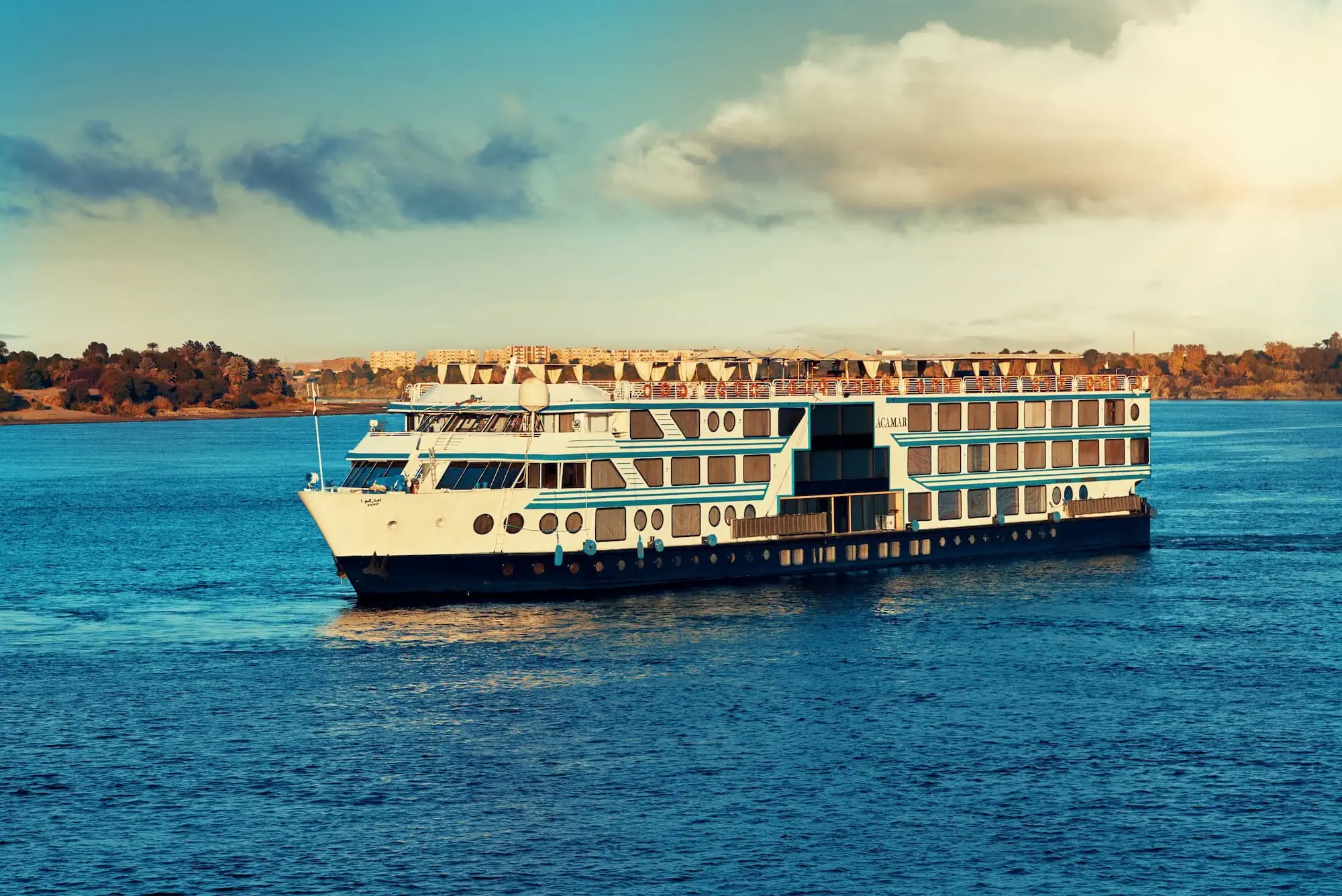 A 5-star Luxury Nile Cruise vessel sailing the Luxor–Aswan stretch of the Nile, carrying 50 to 150 guests with suite cabins and panoramic balconies, the standard cruise inclusion on Luxury Egypt Tour itineraries.