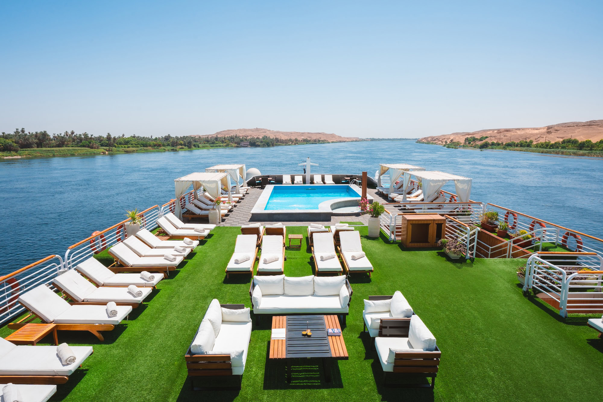 Luxurious Nile River cruise ship deck with swimming pool, lounge chairs and desert hills backdrop
