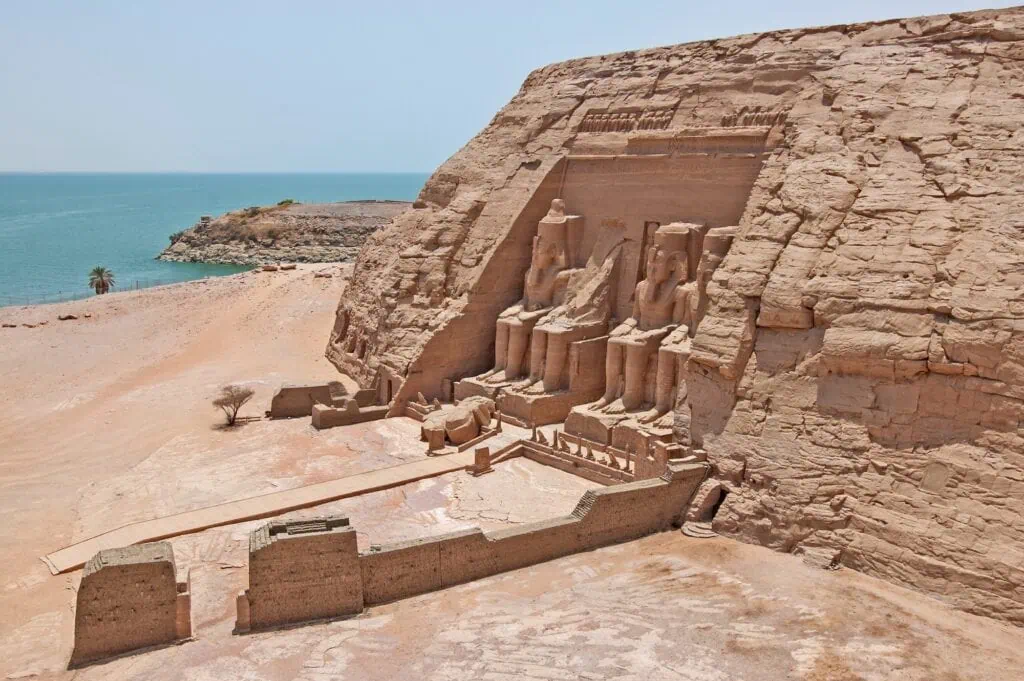 Aerial view of the entrance to the Great Temple of Ramses II at Abu Simbel, southern Egypt — four colossal seated statues of the pharaoh carved into the cliff facade, with Lake Nasser visible in the background - Egypt and Kenya Tours