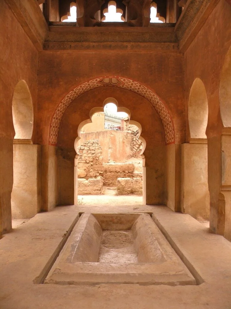 Almoravid Koubba interior with carved arches, central basin, and plaster walls, Marrakesh