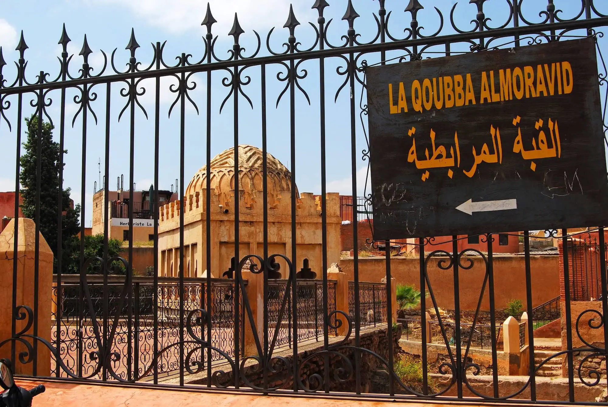 Historic Almoravid Koubba stone dome structure viewed through ornate metal gates in Marrakech