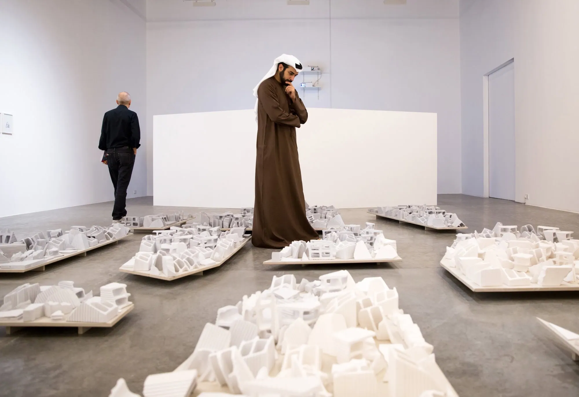 Two men viewing white architectural models in modern art gallery