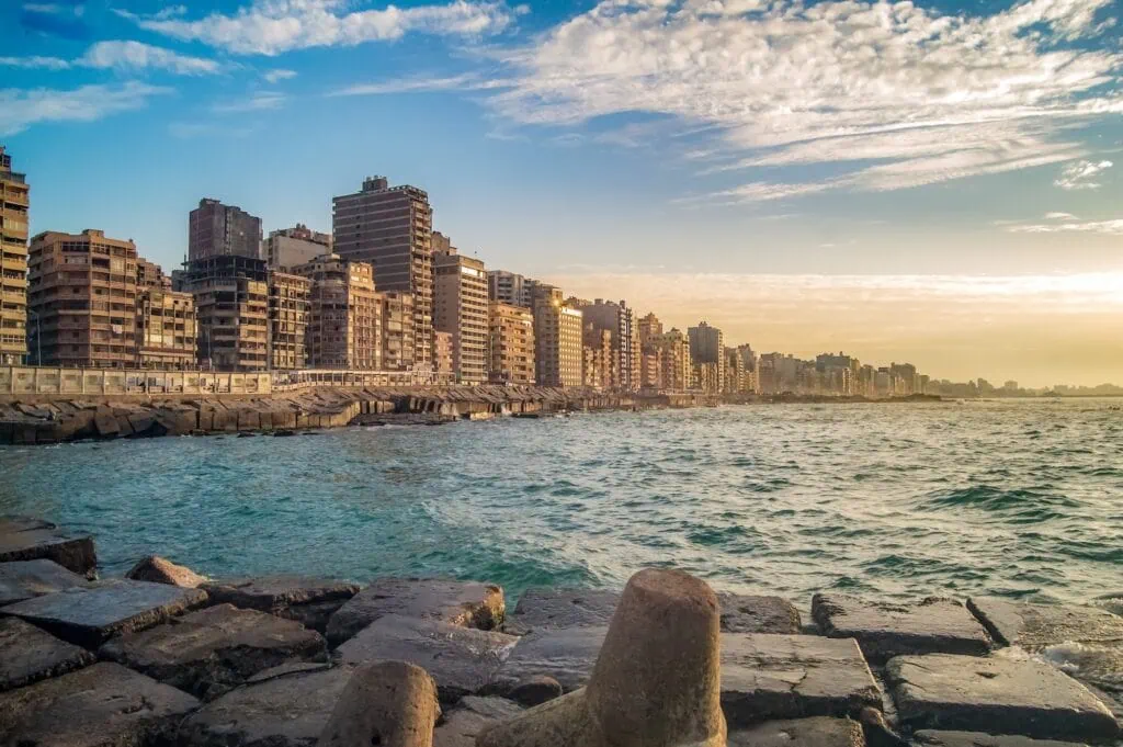 Sunset over the Mediterranean coastline at Alexandria, with the city skyline and waterfront buildings glowing in the evening light, Egypt. Egypt short breaks.