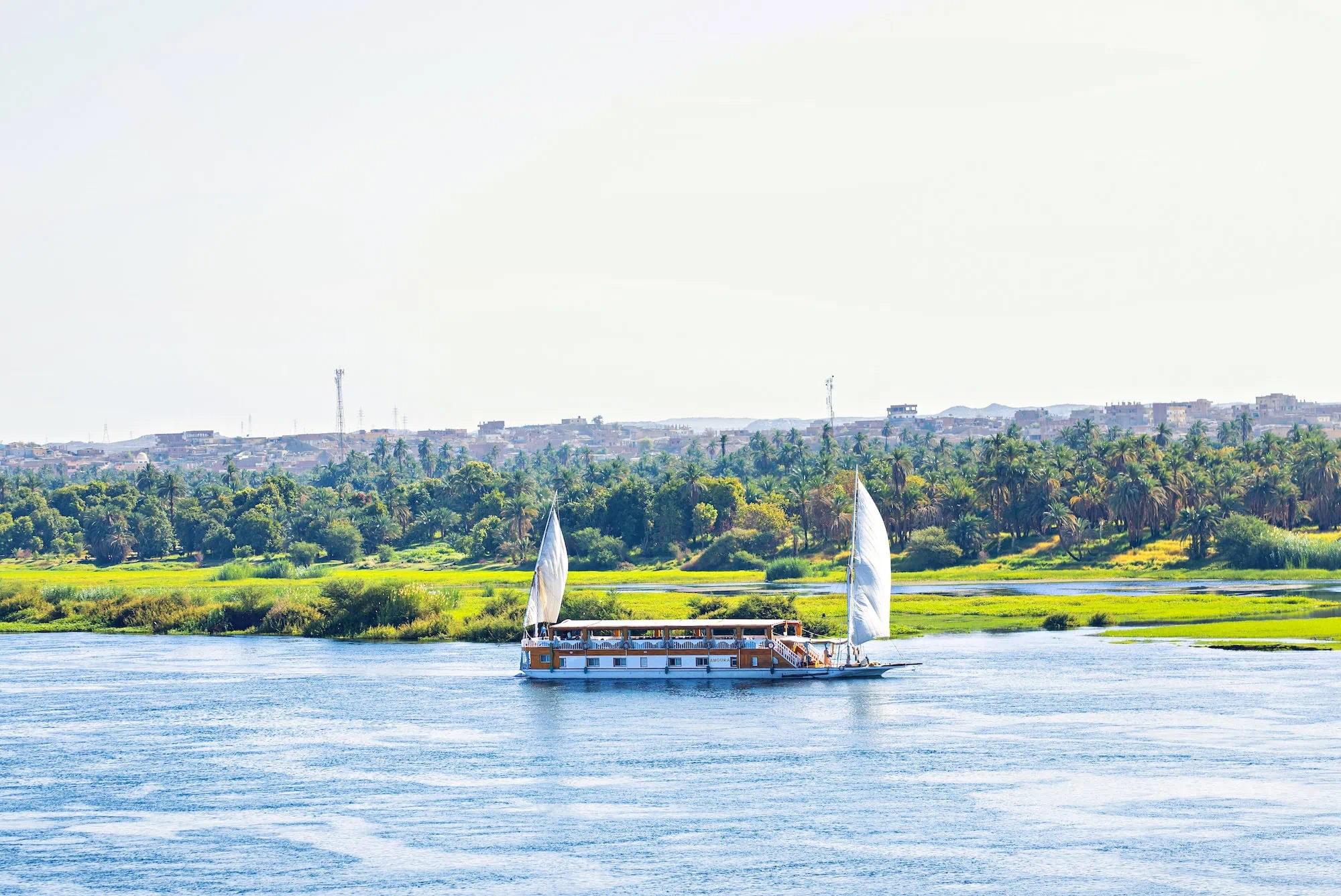A traditional Egyptian dahabiya sailing boat with twin white lateen sails on the Nile River in southern Egypt - Private Nile River Cruises