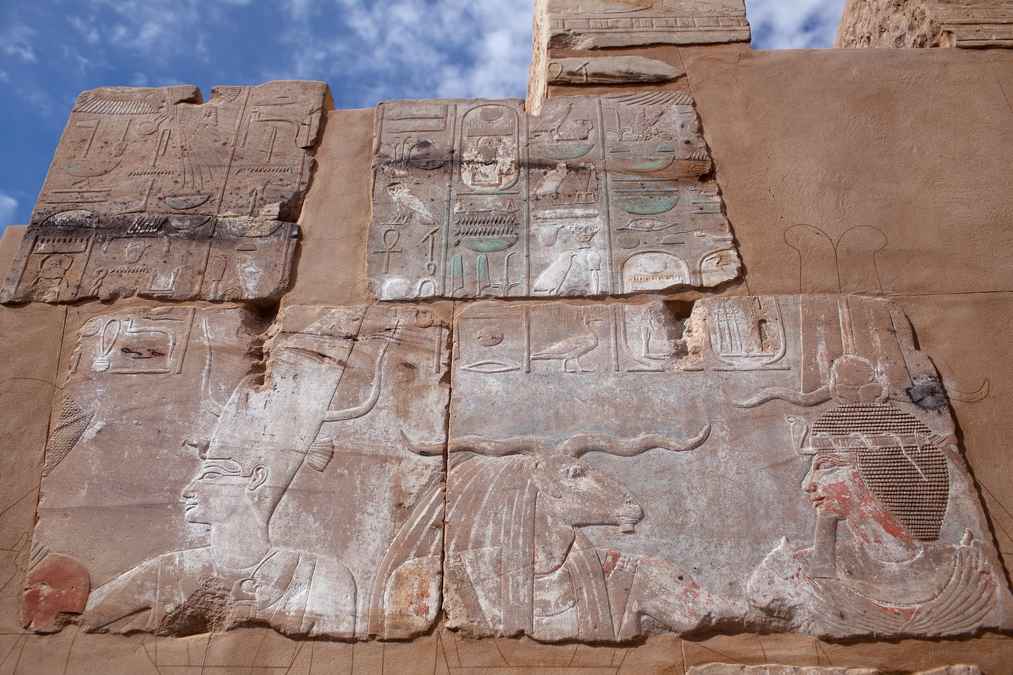 Ancient Egyptian temple wall with hieroglyphics under blue sky with clouds