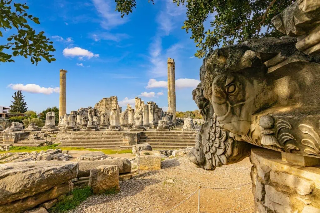 Temple of Apollo with stone columns, stepped platform, and carved head sculpture in Didyma Didim