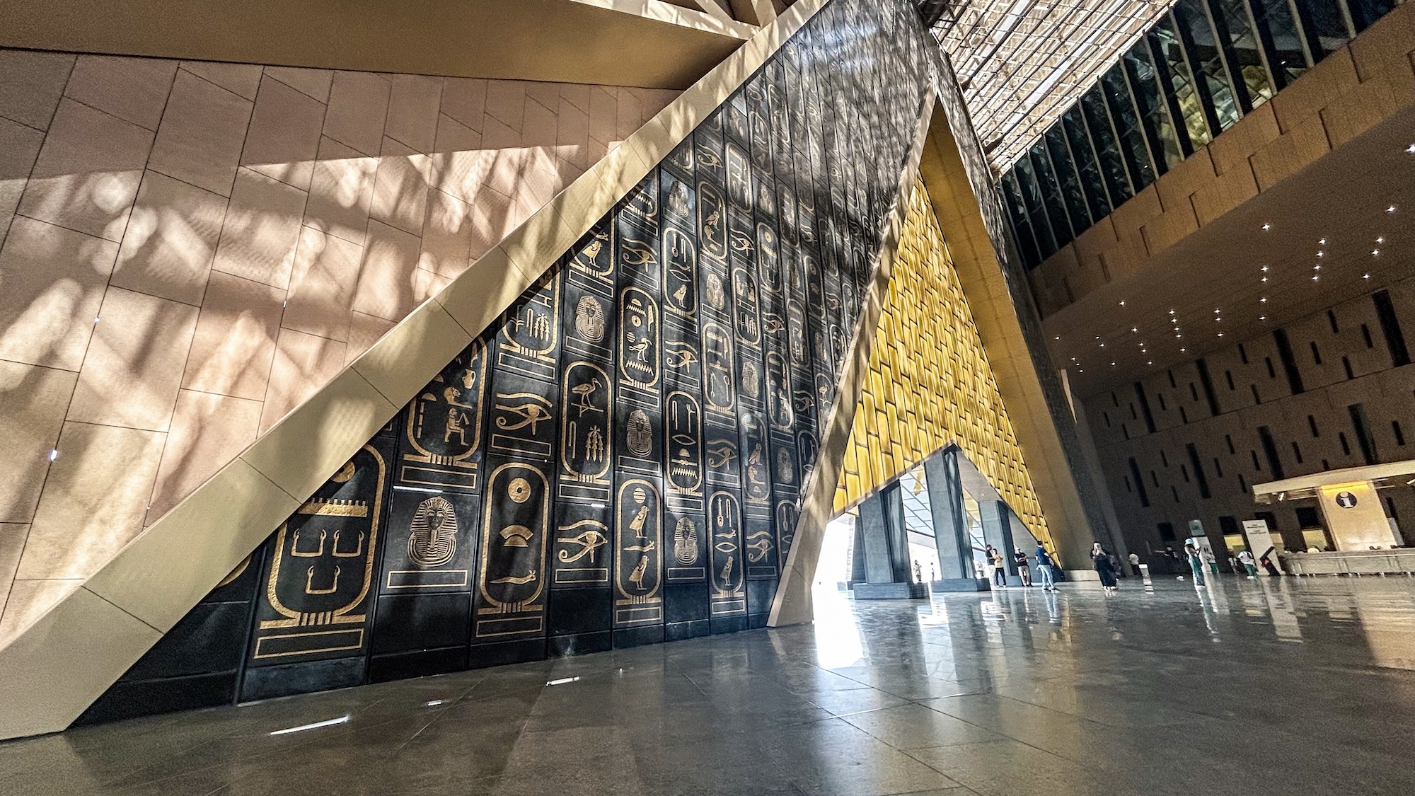 Modern museum interior displaying ancient Egyptian hieroglyphs and pharaoh artifacts with visitors exploring