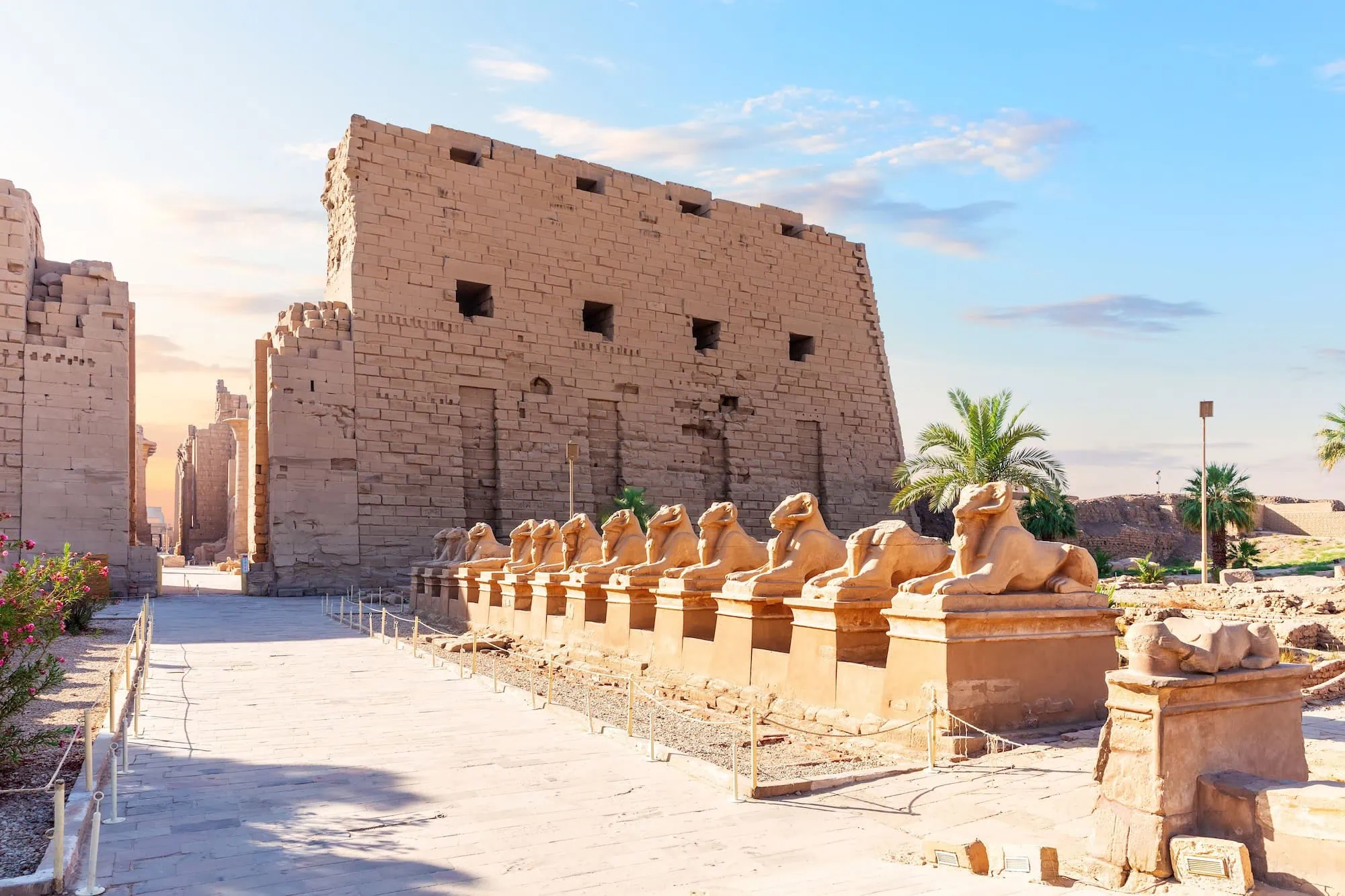 Row of ram-headed sphinx statues leading to the massive Karnak Temple Complex with towering columns and ancient walls