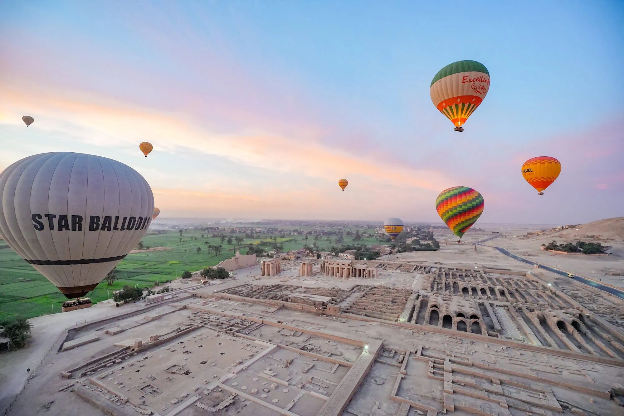 Hot air balloons floating at sunrise above an ancient temple complex on the west bank at Luxor, Egypt.