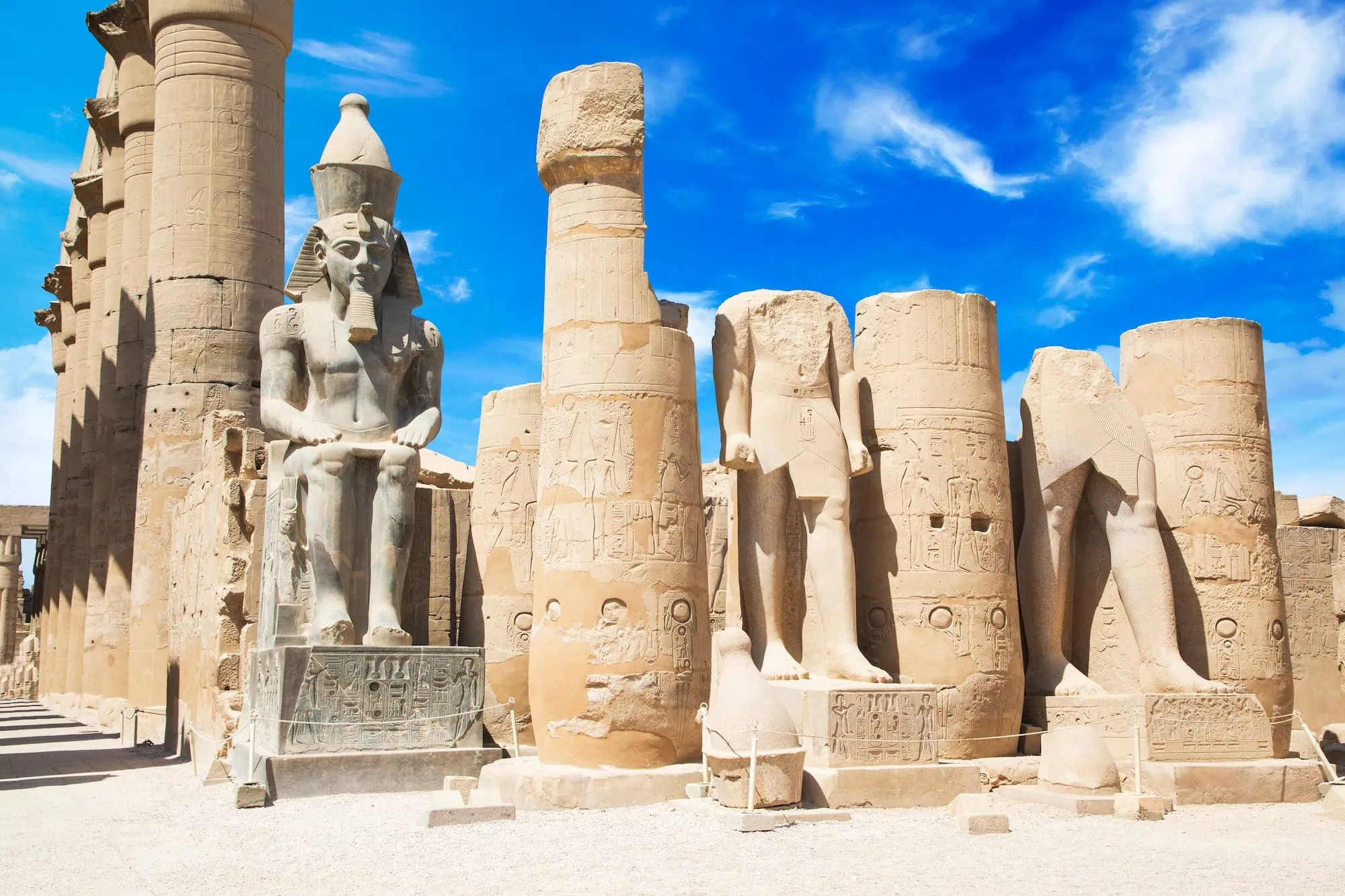 Ram-headed sphinx and pharaoh statues among hieroglyphic-covered columns at the Karnak Temple Complex in Luxor.