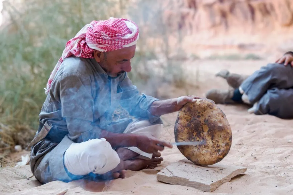 Bedouin man baking traditional flatbread over an open desert fire