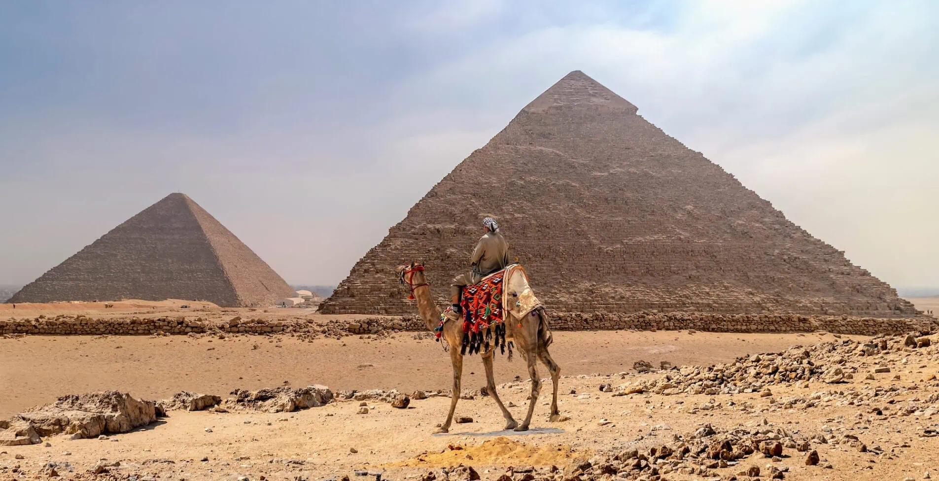 Bedouin on camel in the area with the great pyramids of Giza Egypt 1905x976 crop 46 67