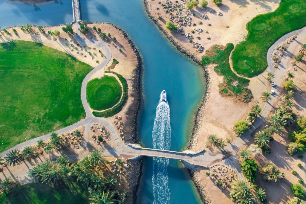 Aerial view of lagoon-side golf course with small boat crossing waterways