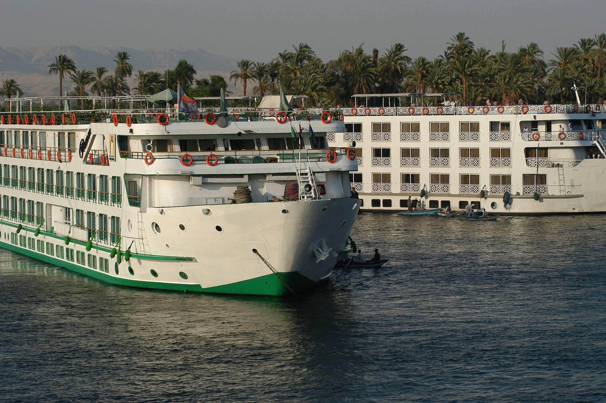 Nile River cruise ships docked along the riverbank with mountains in background
