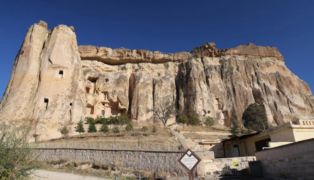Cavusin Church carved into a rock hillside with arched openings and weathered stone walls in Nevsehir City
