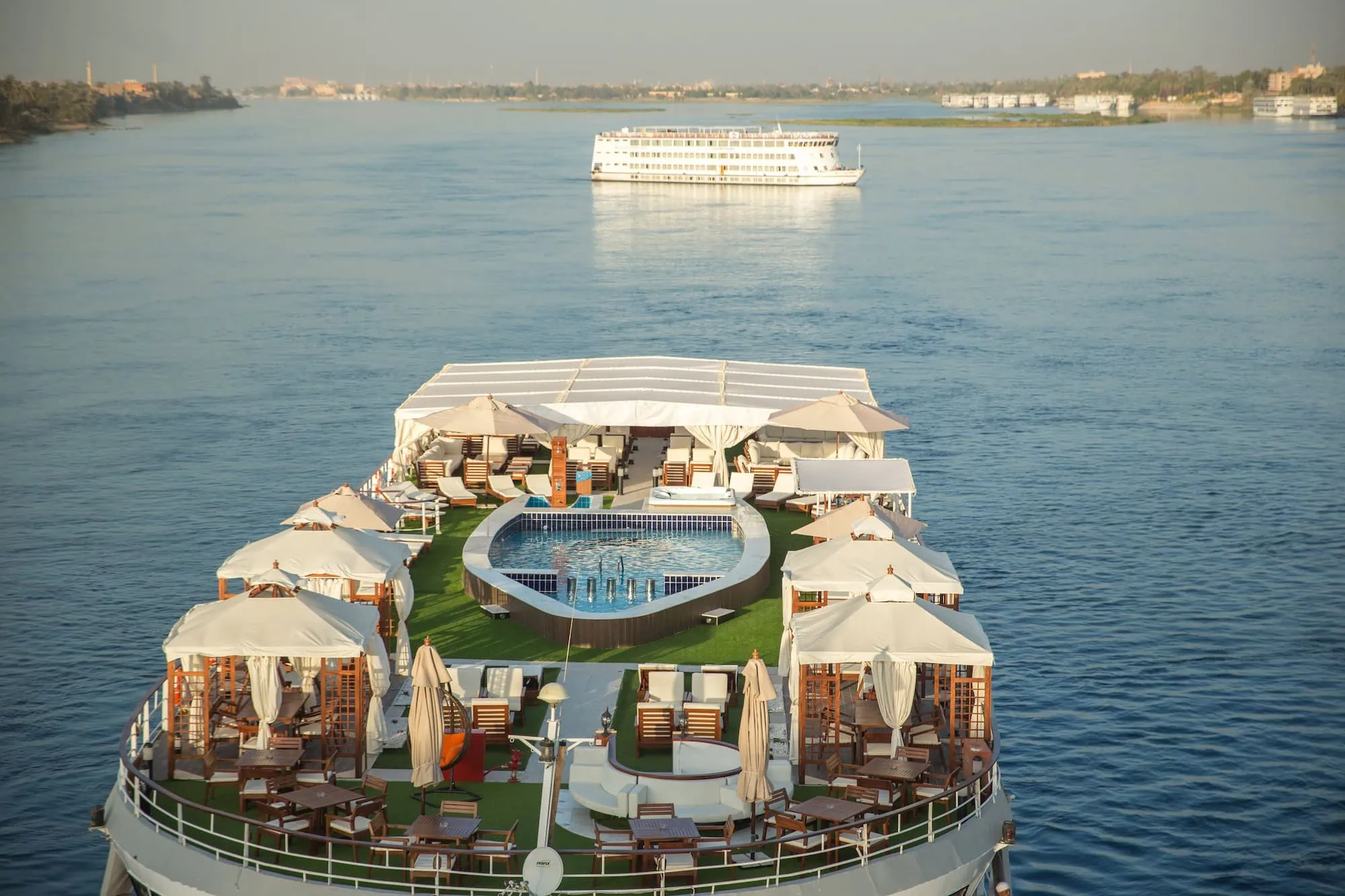 An aerial view of a modern Luxury Nile Cruise vessel with a swimming pool on its sun deck, sailing the Nile River between Luxor and Aswan, Egypt.