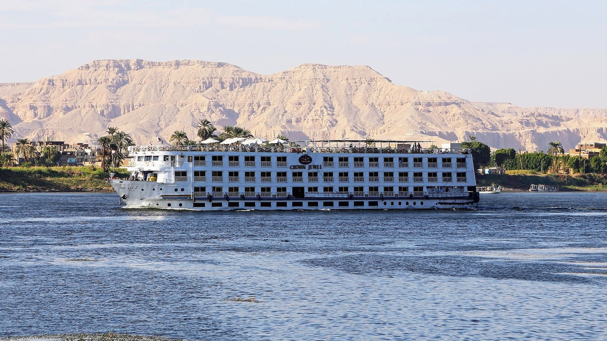 Nile River cruise ship sailing past desert cliffs and palm trees in Egypt