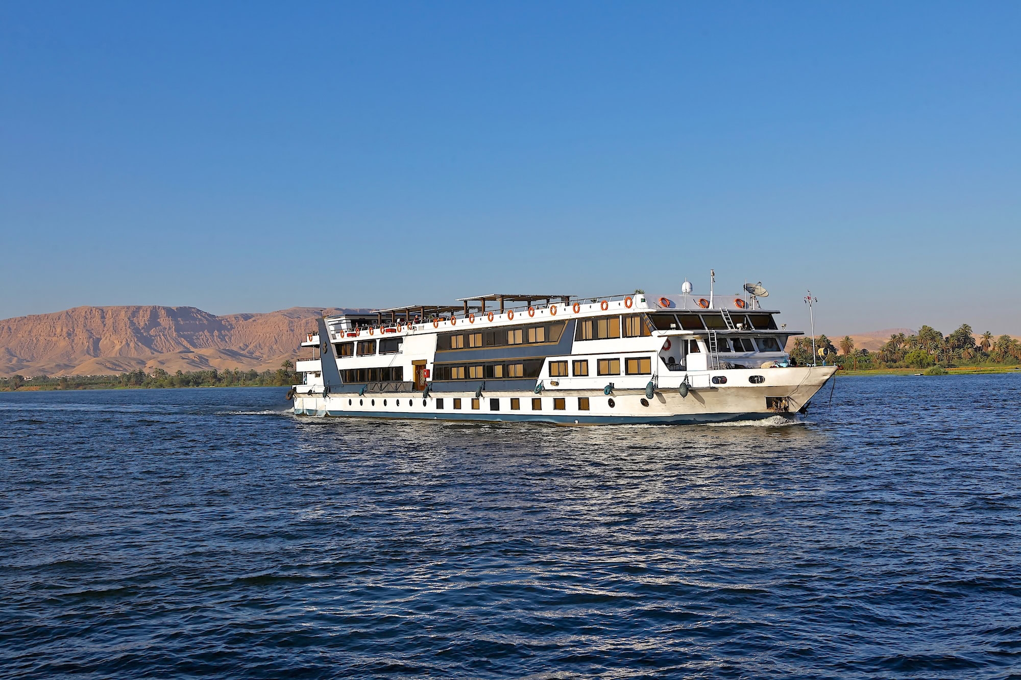 Navio de cruzeiro navegando pelo Rio Nilo entre montanhas desérticas no Egito