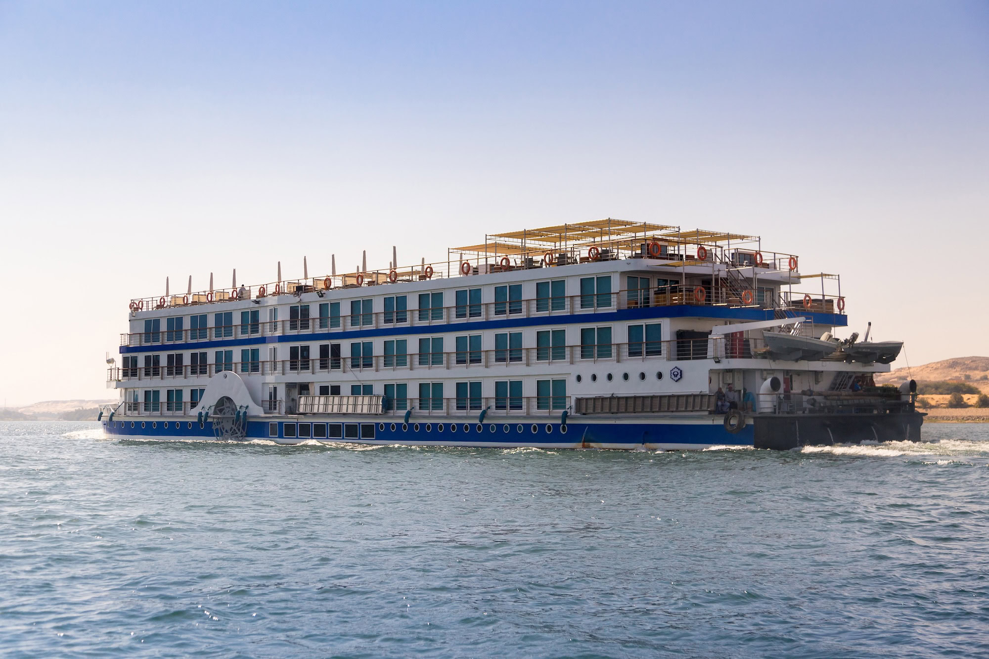 Large multi-deck Nile River cruise ship sailing on the Nile with desert landscape in background