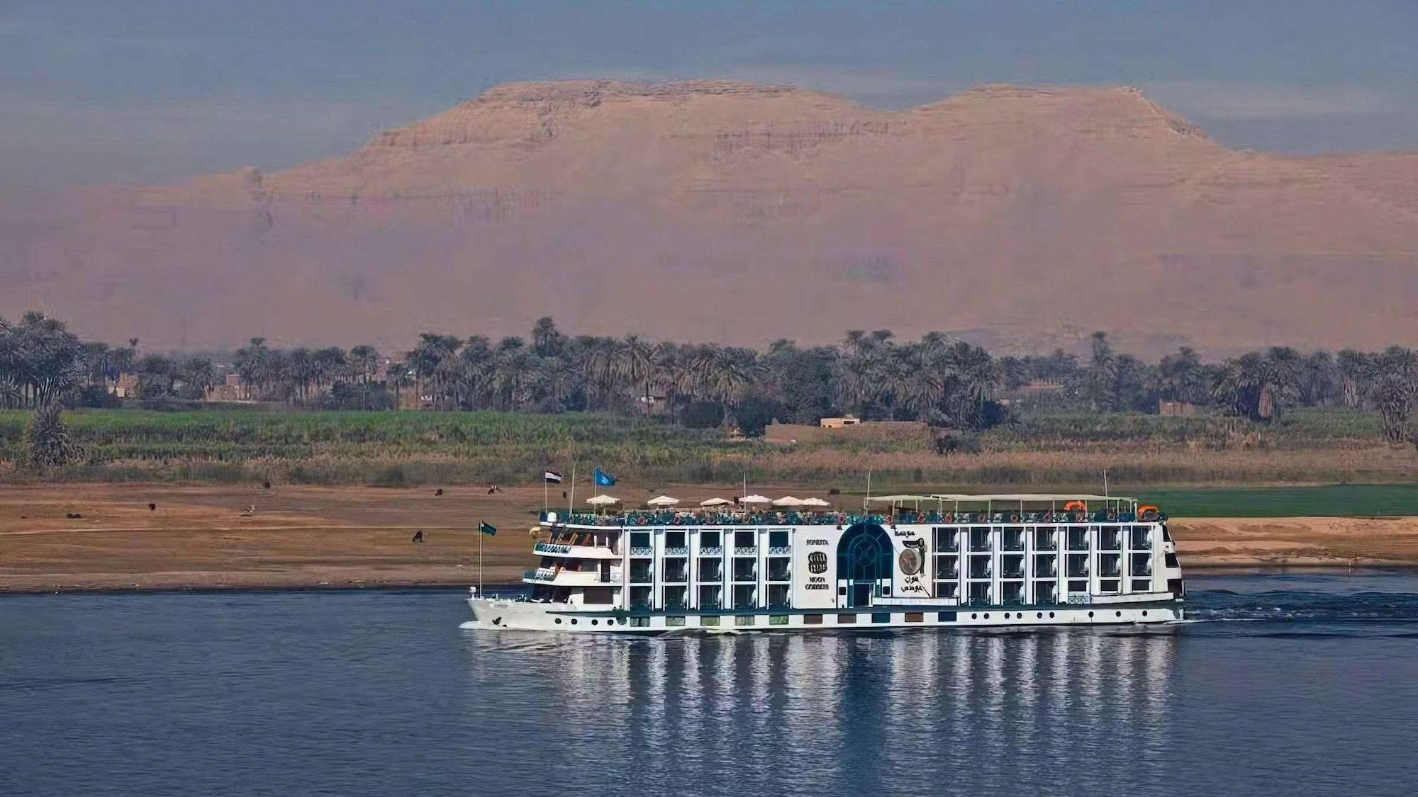 Large cruise ship on the Nile River with desert cliffs and vegetation