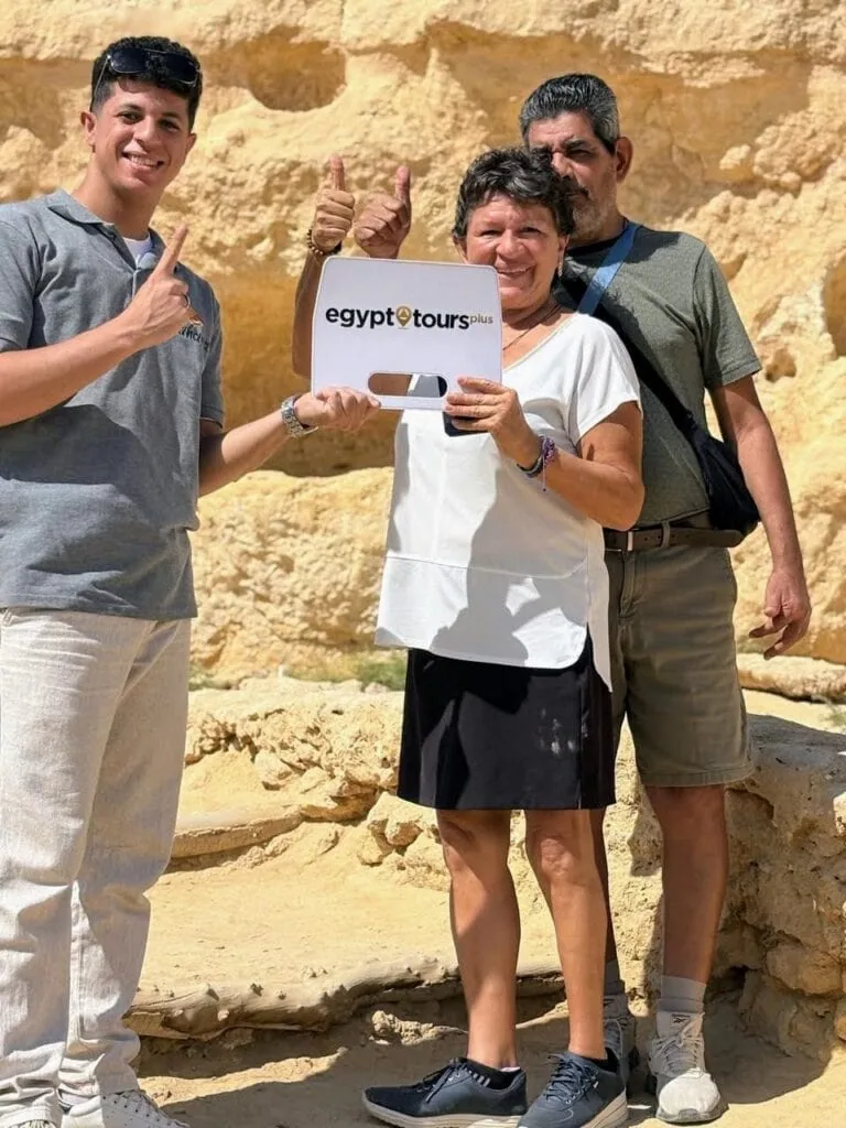 Happy customers posing with a tour guide holding an Egypt Tours Plus sign in a desert setting, Giza