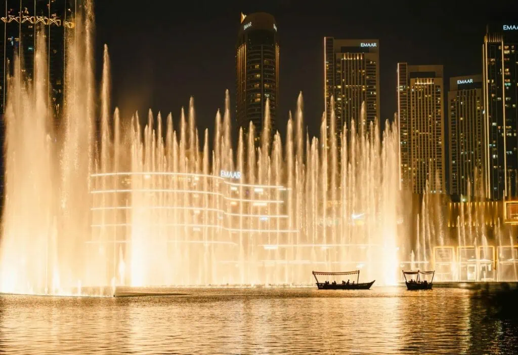 Dubai Fountain illuminated water jets rising from Burj Lake with boats and Emaar towers in the background Dubai