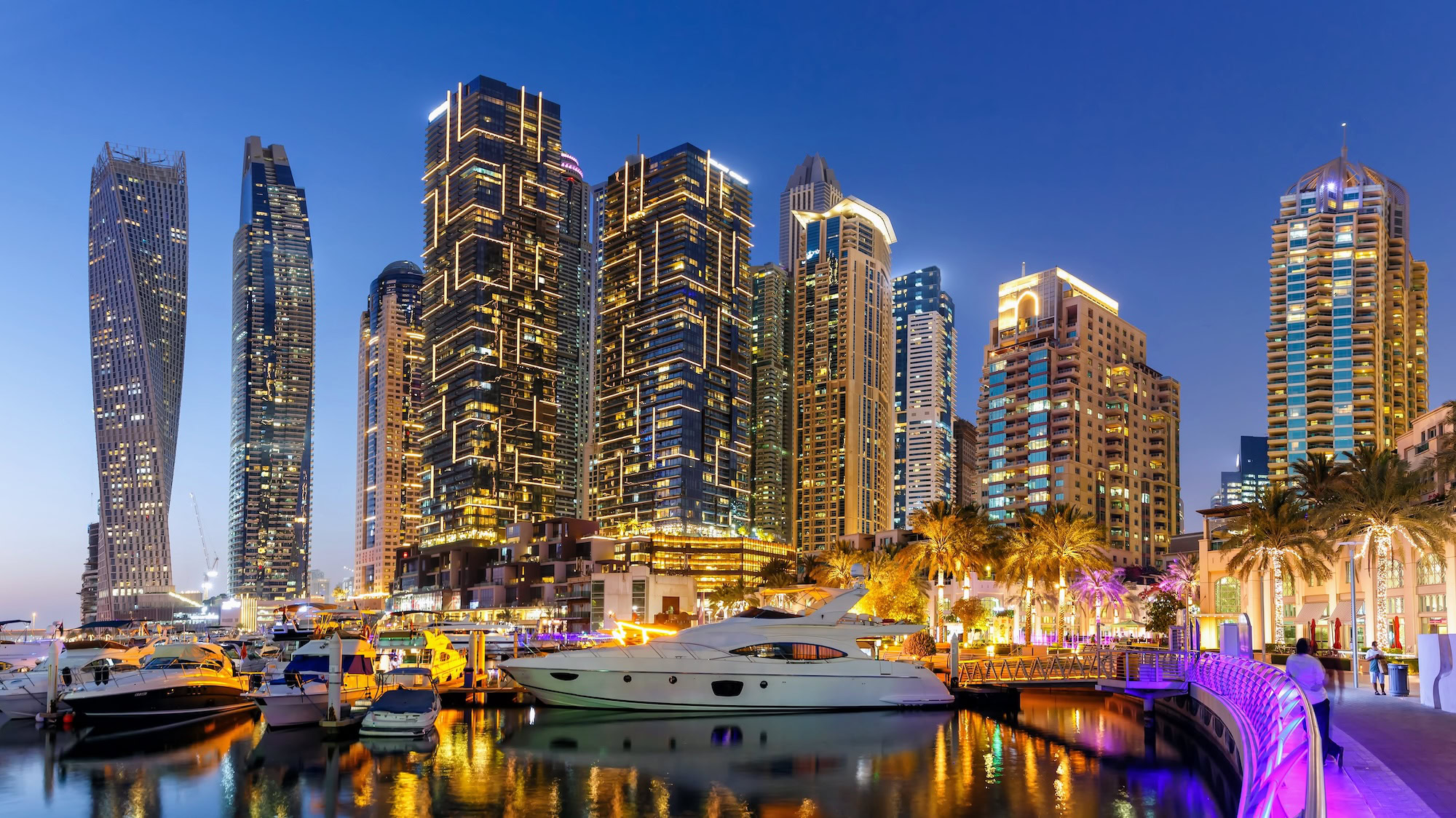 Dubai Marina with illuminated skyscrapers, yachts, and boats reflecting in the water at evening