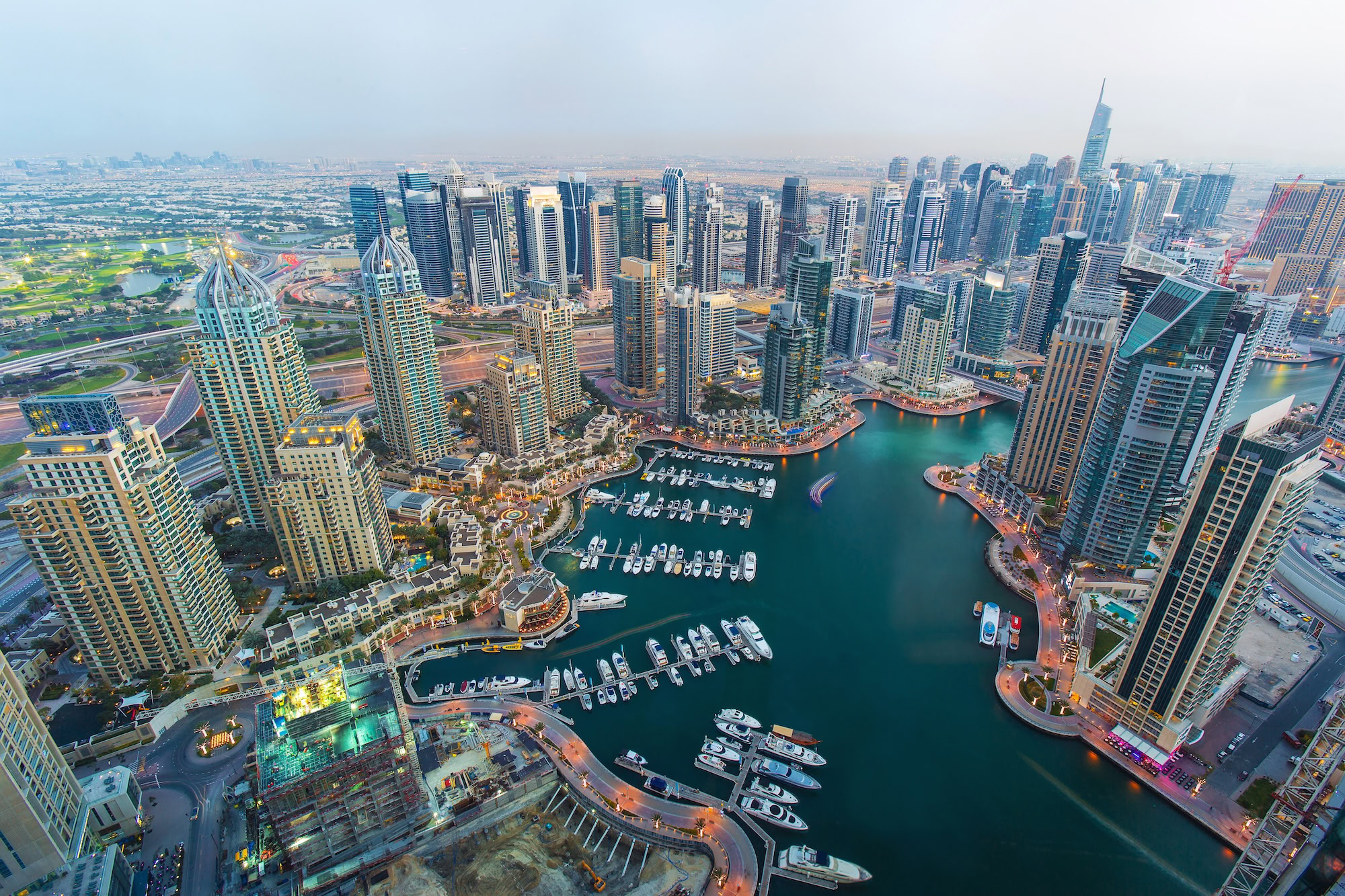 Aerial view of Dubai Marina showing towering skyscrapers, marina with boats, and urban waterfront development