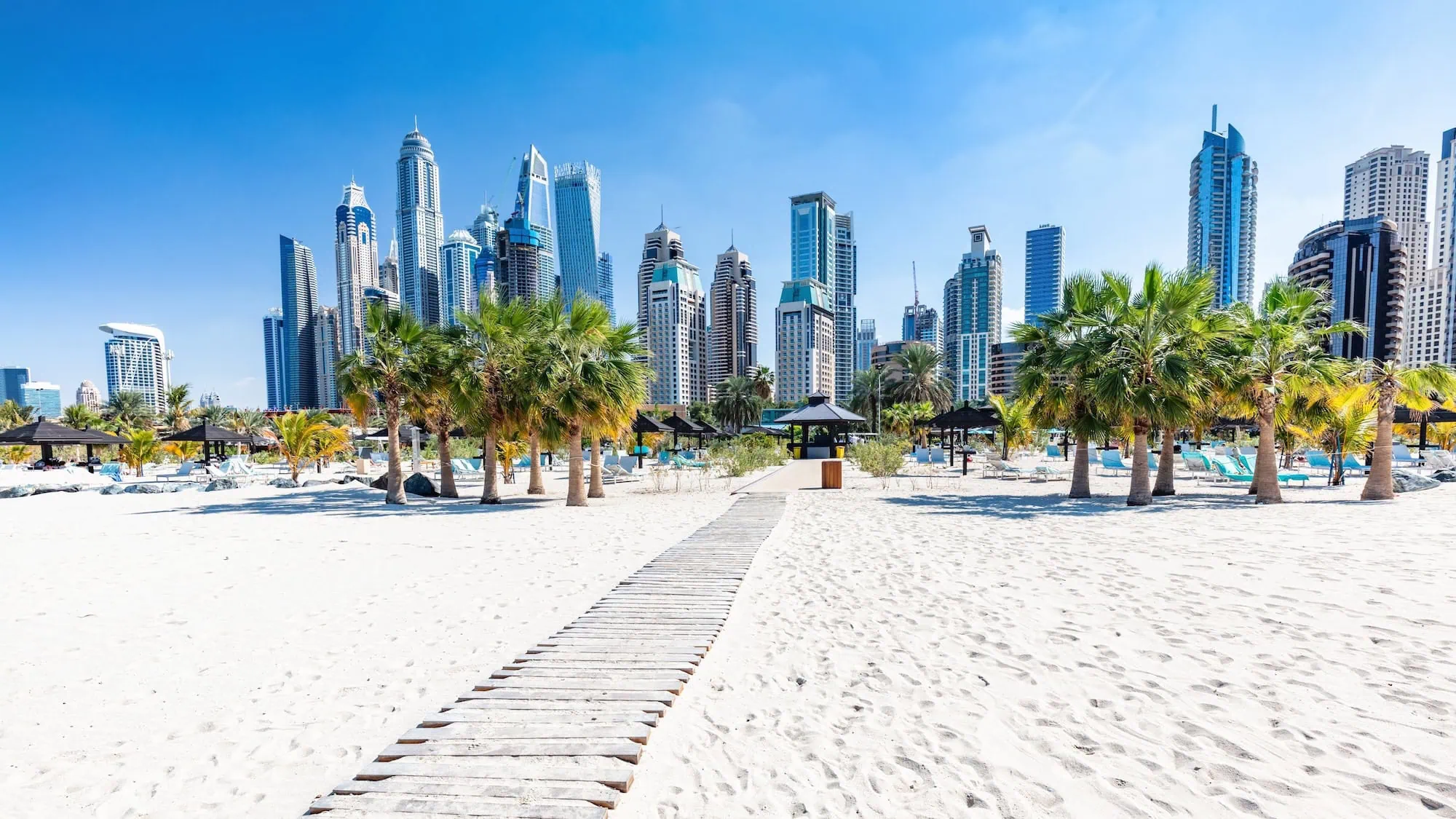 Jumeirah Beach with white sand, palm trees and Dubai Marina skyline in background
