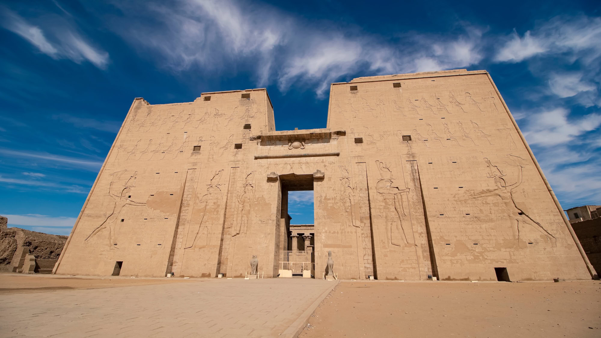 Temple of Edfu entrance with massive sandstone pylon, hieroglyphic carvings, and ancient courtyard