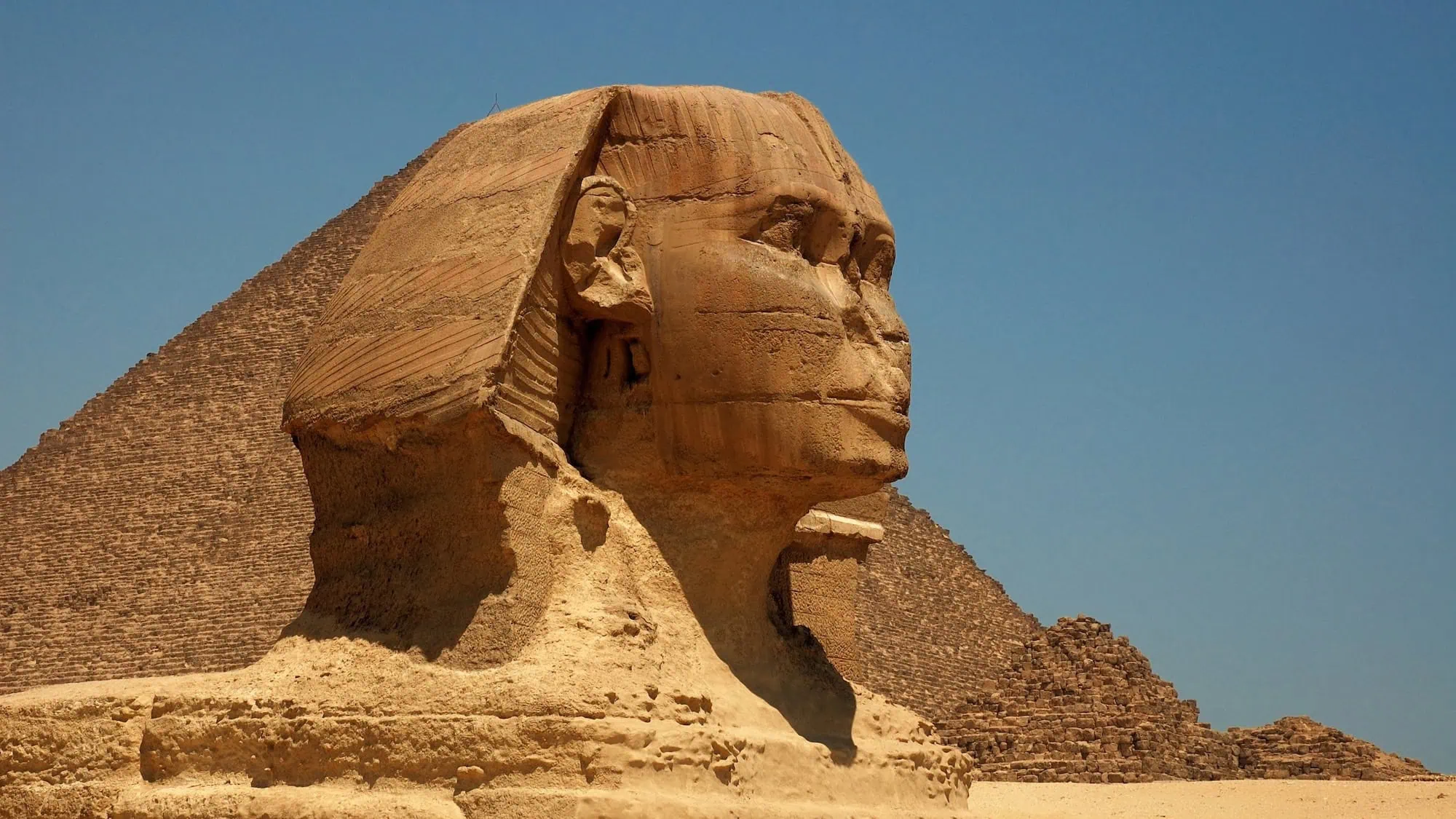 The Great Sphinx of Giza with pyramid in background under clear blue sky