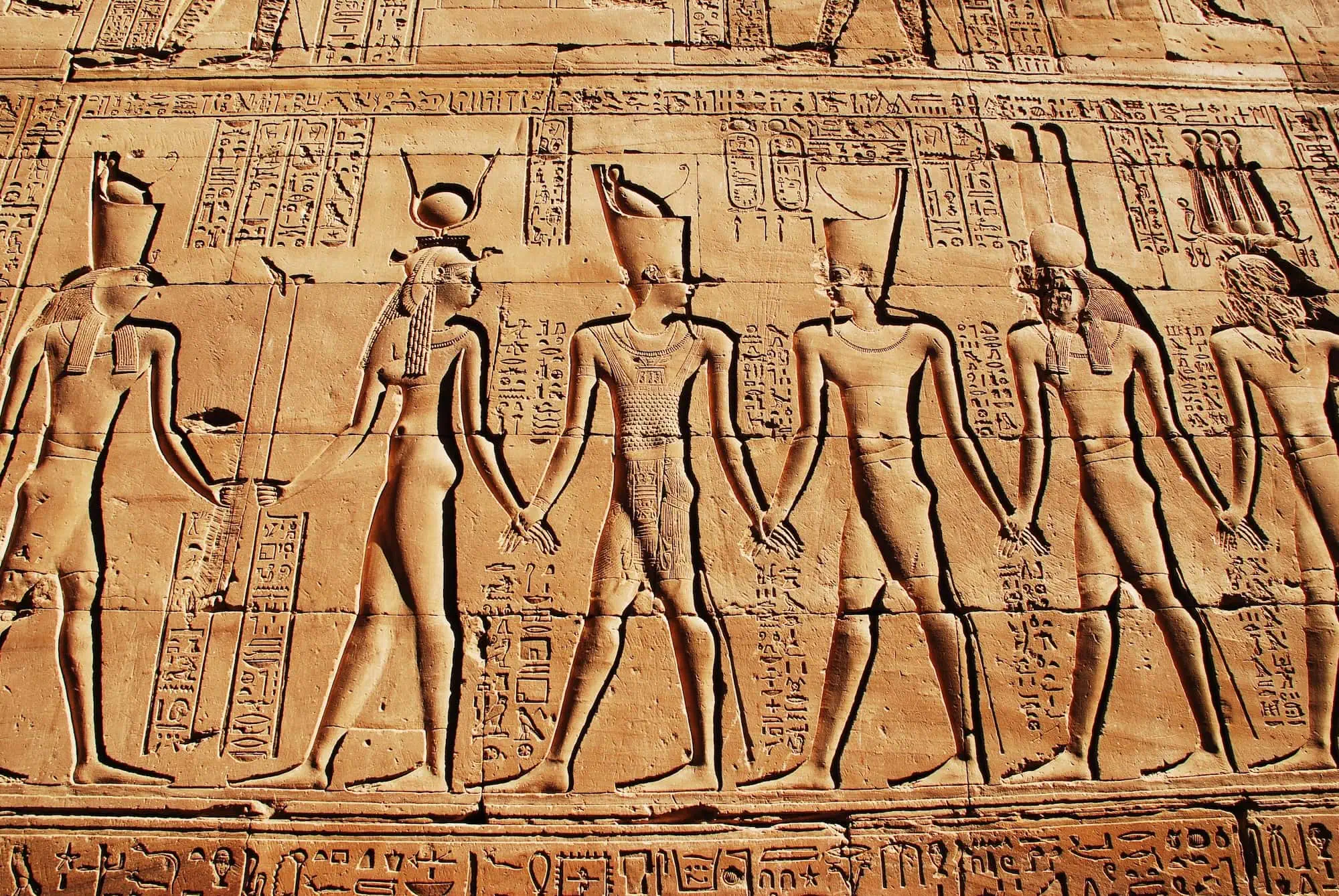 Ancient Egyptian temple wall relief with detailed hieroglyphic texts and carved figures of deities