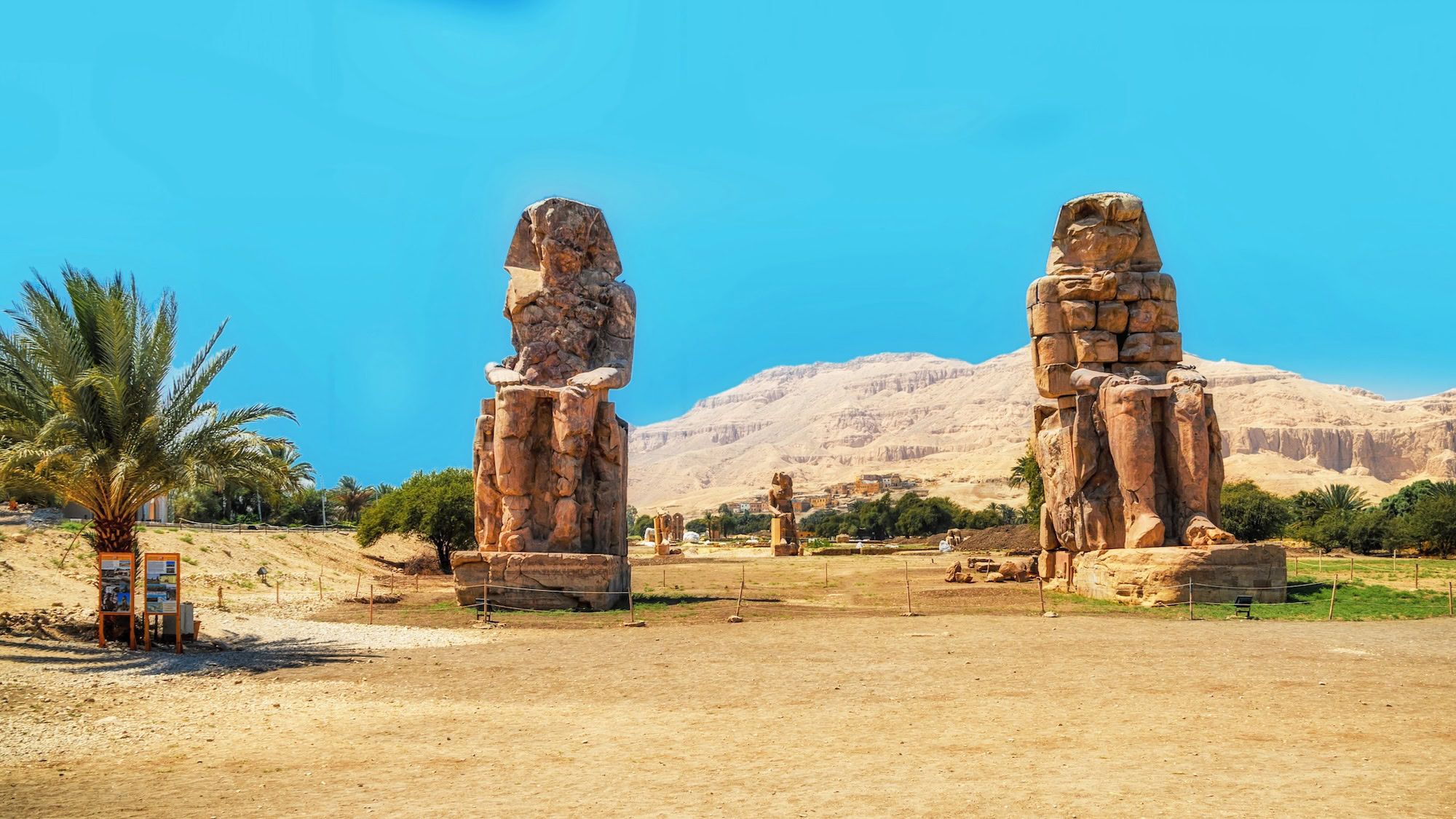Majestic view of the ancient Colossi of Memnon statues against desert mountains