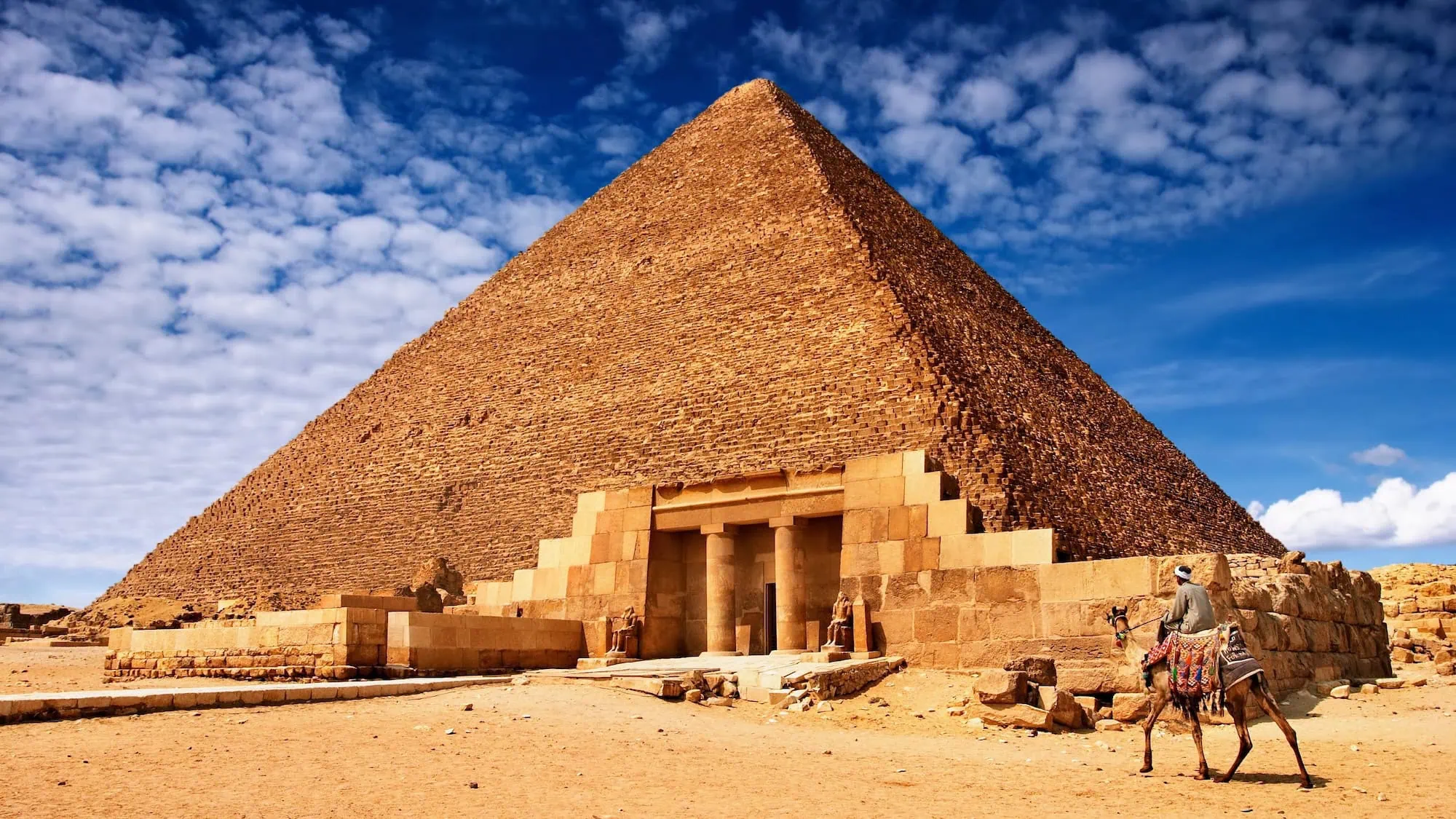 Egyptian pyramid with camel rider under clear blue skies and sunny weather - Egypt Christmas Tours