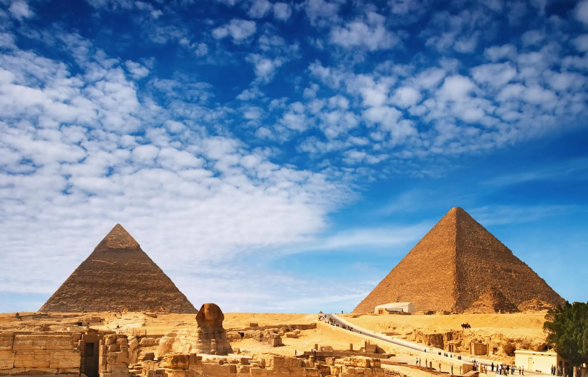 Panoramic view of Giza pyramids and Great Sphinx with tourists on walkways
