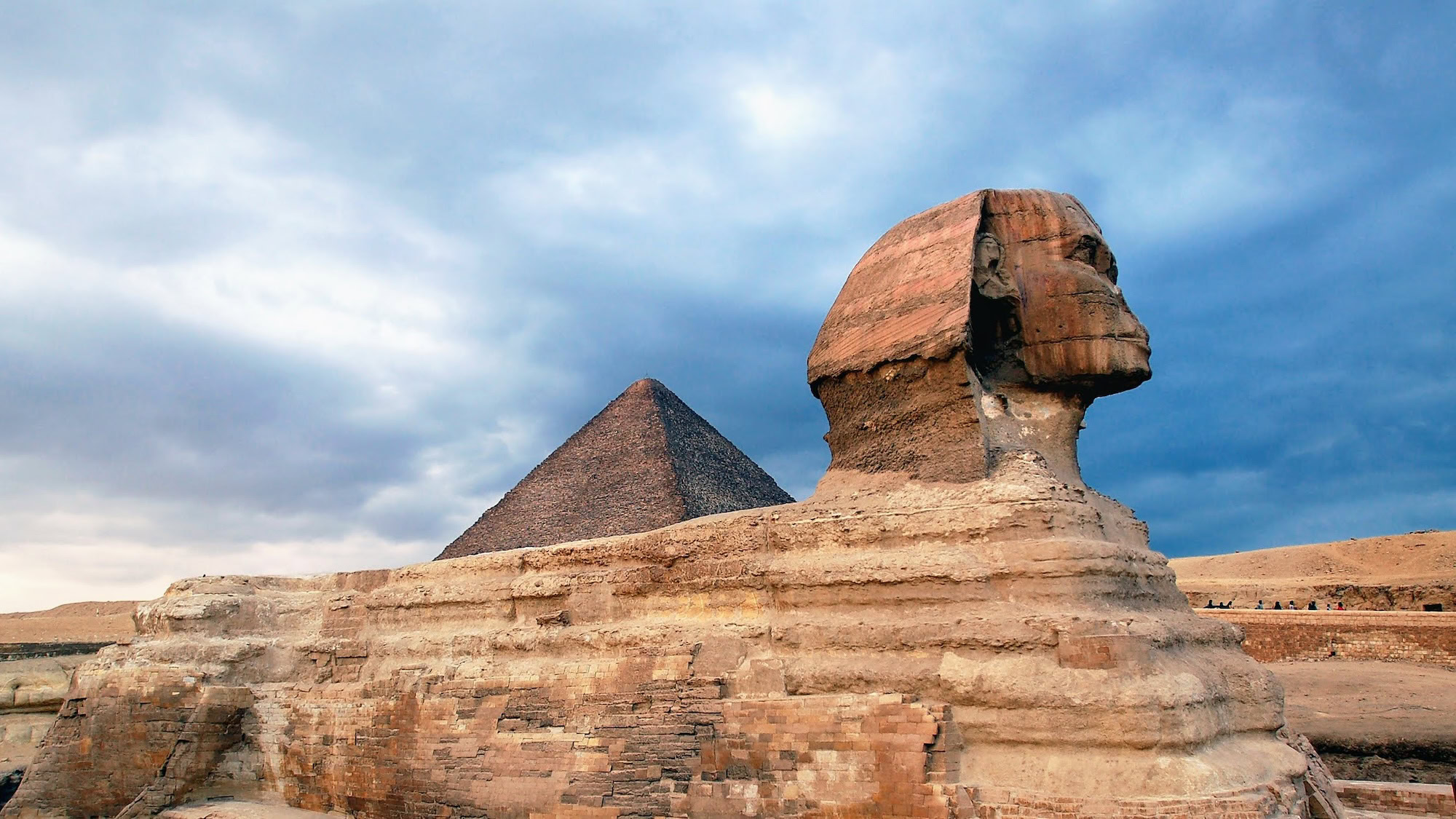 The Great Sphinx of Giza with pyramid in background under cloudy sky