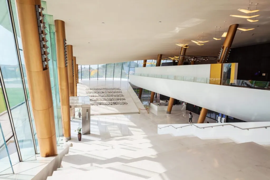 Etihad Museum interior hall with sloped floor displaying Arabic inscriptions, tall columns, and glass walls Dubai