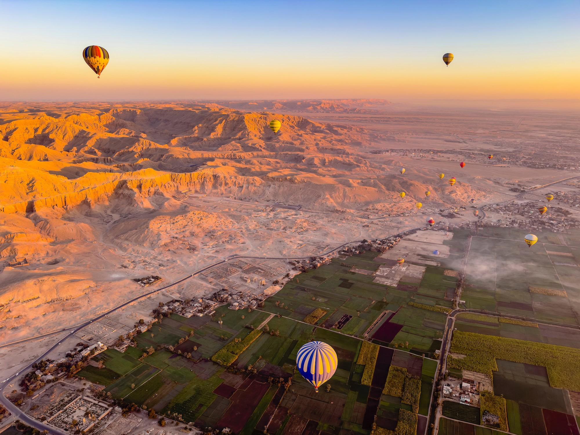 Aerial view of Luxor's Valley of the Kings with hot air balloons over desert mountains and agricultural fields