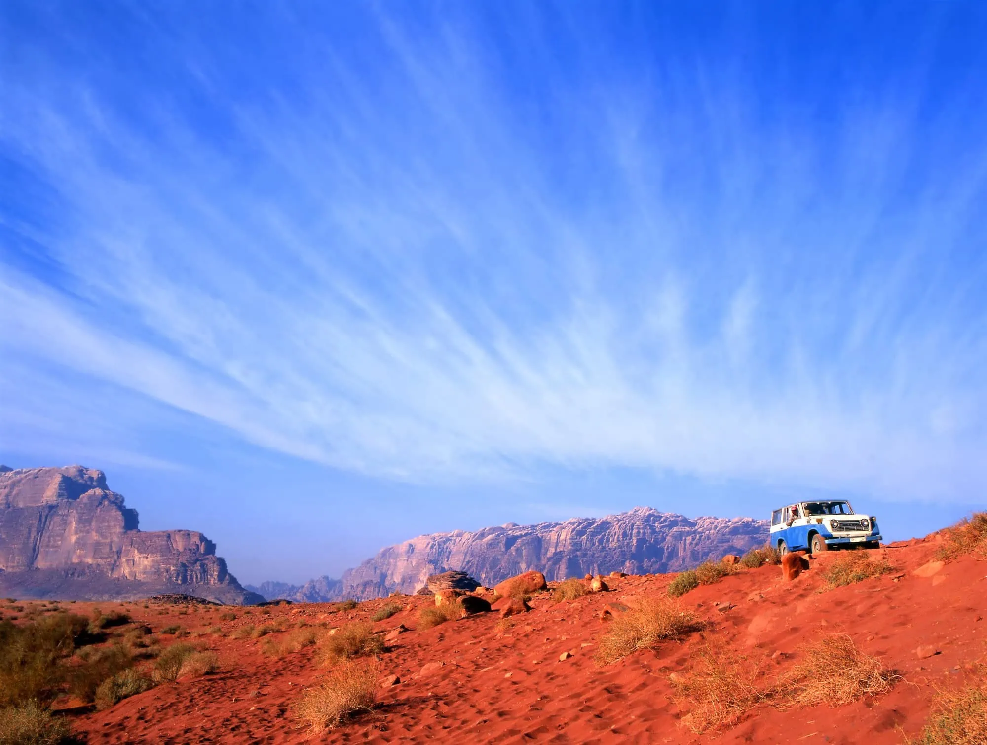 White four-wheel drive vehicle on red sand dunes in Wadi Rum desert