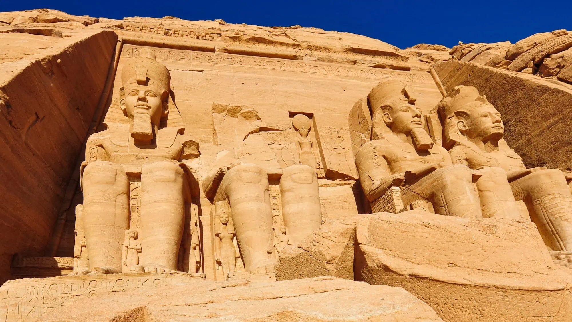 The four colossal seated statues of Ramses II at the entrance of the Great Temple of Abu Simbel, carved into the sandstone cliff - Aswan Tours