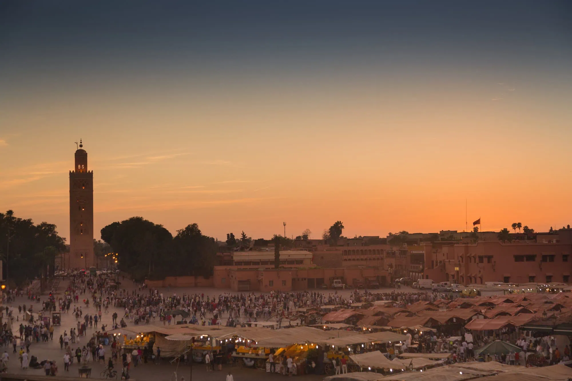 Jemaa el-Fnaa square at dusk with the Koutoubia Mosque minaret in the distance, the historic heart of the Marrakech medina.